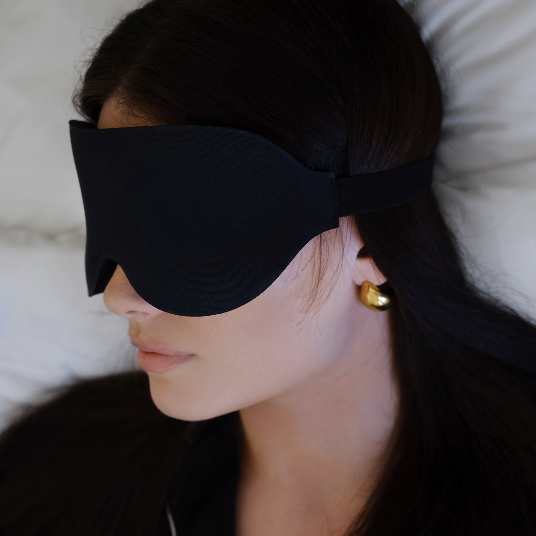 Sovemaske i mykt materiale brukt under søvn i seng med lyst sengetøy